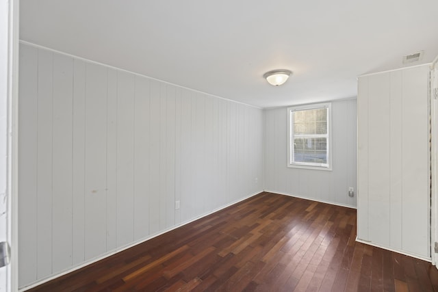 unfurnished room with dark wood-type flooring and wooden walls