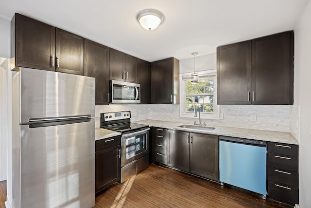 kitchen featuring sink, hanging light fixtures, light stone counters, dark hardwood / wood-style floors, and appliances with stainless steel finishes