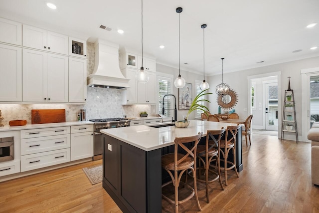 1903 Bolden Dr, Mount Pleasant, SC 29466 - kitchen with custom exhaust hood, a kitchen island with sink, tasteful backsplash, a kitchen breakfast bar, and light wood-style floors
