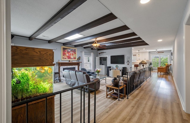 living room with beam ceiling, ceiling fan, light wood-style floors, a fireplace, and baseboards