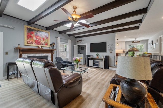 living room with a fireplace, ceiling fan, plenty of natural light, light wood-style flooring, and beamed ceiling