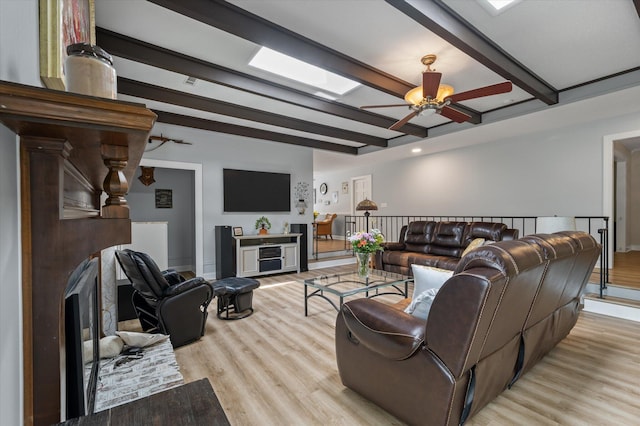 living area with beam ceiling, light wood-style floors, ceiling fan, baseboards, and a skylight