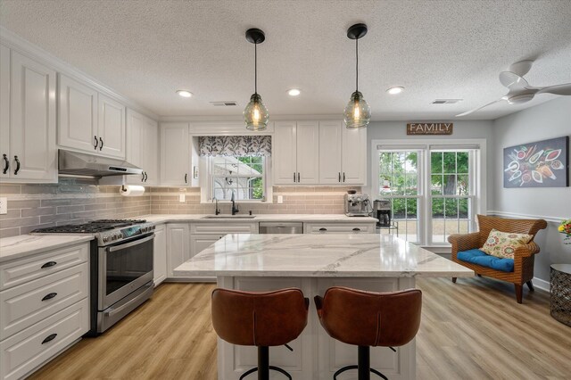 kitchen featuring stainless steel appliances, under cabinet range hood, a sink, white cabinets, and a textured ceiling