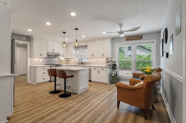 kitchen with appliances with stainless steel finishes, a textured ceiling, white cabinets, backsplash, and under cabinet range hood