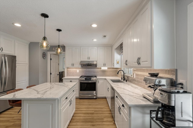 kitchen with stainless steel appliances, a sink, under cabinet range hood, white cabinets, and backsplash