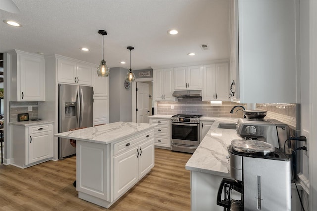 kitchen featuring stainless steel appliances, a sink, under cabinet range hood, a center island, and tasteful backsplash