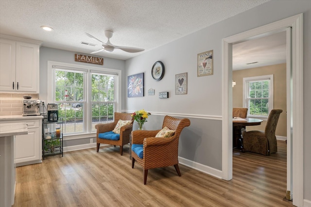 living area featuring light wood-type flooring, ceiling fan, baseboards, and a textured ceiling