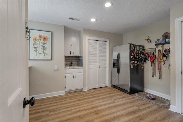 kitchen featuring stainless steel refrigerator with ice dispenser, light wood-type flooring, white cabinetry, baseboards, and decorative backsplash