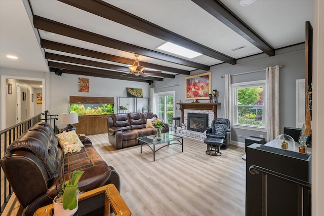 living area featuring wood finished floors, a brick fireplace, beam ceiling, ceiling fan, and baseboards