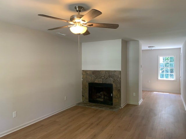 unfurnished living room with visible vents, a ceiling fan, a stone fireplace, wood finished floors, and baseboards