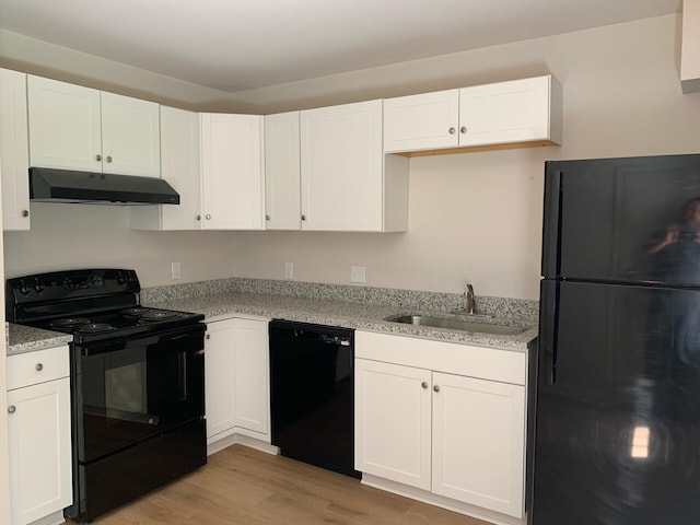 kitchen featuring light wood finished floors, white cabinets, under cabinet range hood, black appliances, and a sink