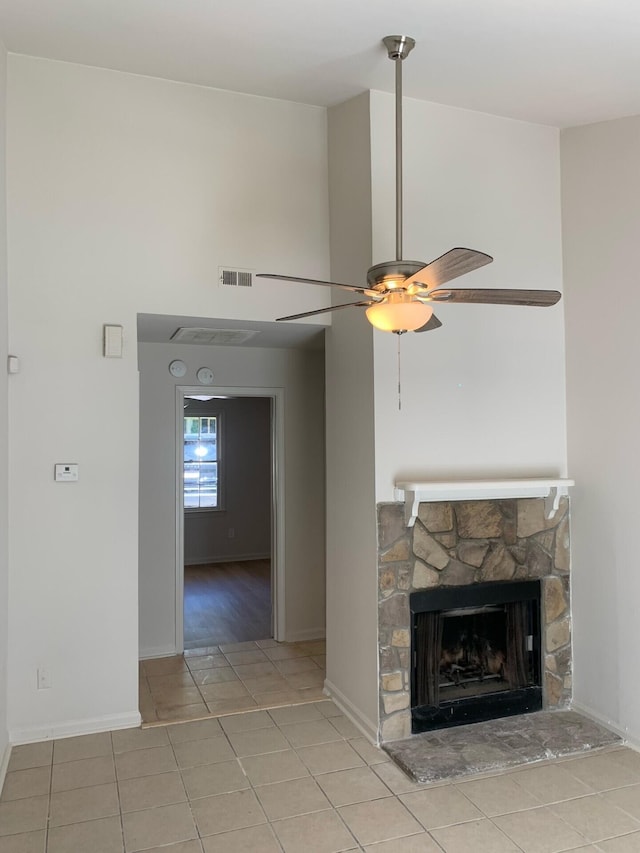 unfurnished living room featuring light tile patterned flooring, a fireplace, a towering ceiling, visible vents, and a ceiling fan