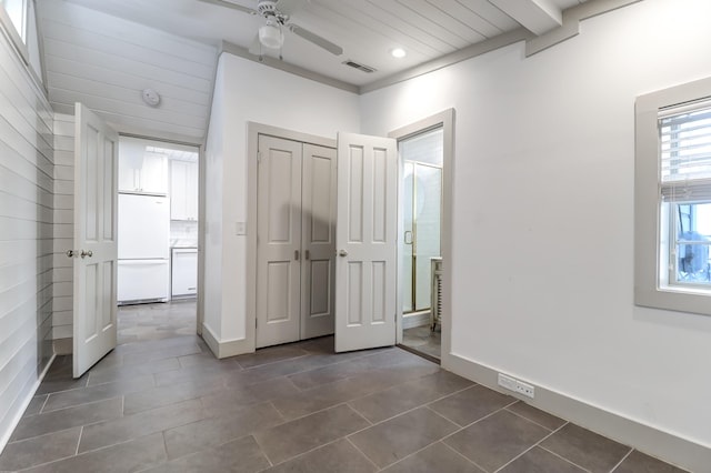 unfurnished bedroom featuring white refrigerator, a closet, ceiling fan, and dark tile floors