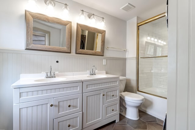 full bathroom with tile flooring, double sink vanity, toilet, and bath / shower combo with glass door