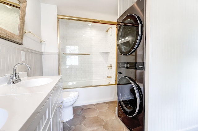 full bathroom with vanity with extensive cabinet space, shower / bath combination with glass door, tile flooring, stacked washing maching and dryer, and toilet