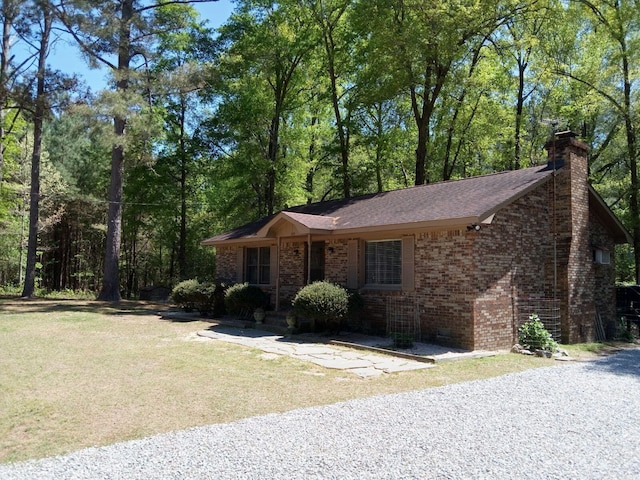 ranch-style house with brick siding, a chimney, a front yard, and a shingled roof