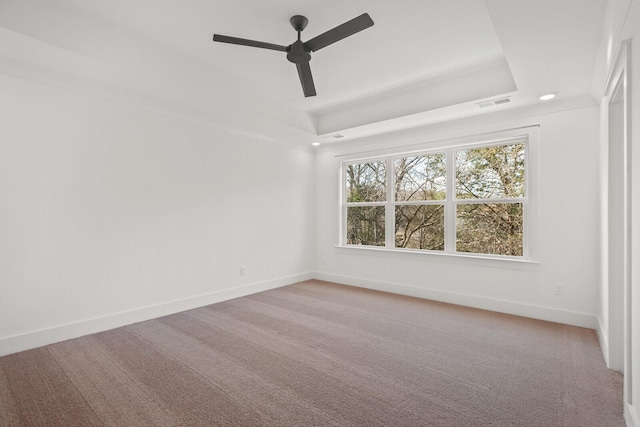 carpeted empty room with a tray ceiling, baseboards, visible vents, and a ceiling fan