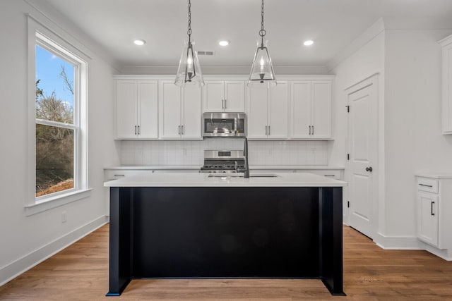 kitchen featuring a kitchen island with sink, light wood-type flooring, stainless steel appliances, and white cabinets