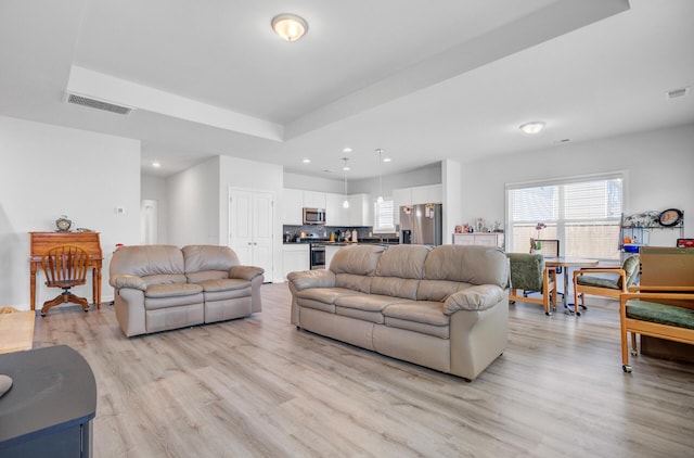 living area with light wood-style flooring, recessed lighting, and a tray ceiling