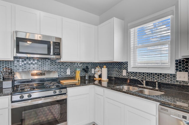 kitchen with stainless steel appliances, a sink, white cabinetry, backsplash, and dark stone countertops