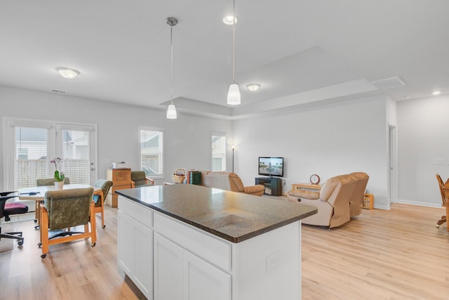 kitchen with dark countertops, light wood-style floors, a kitchen island, white cabinets, and pendant lighting