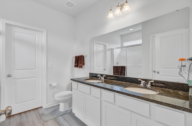 bathroom featuring a stall shower, toilet, wood finished floors, double vanity, and baseboards