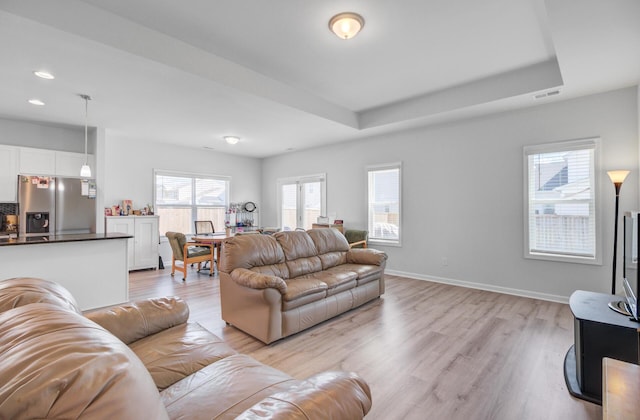 living room with light wood-type flooring, a tray ceiling, recessed lighting, and baseboards