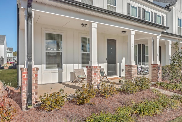 doorway to property featuring covered porch, board and batten siding, and brick siding