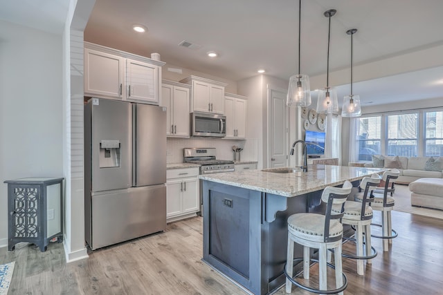 kitchen featuring stainless steel appliances, a sink, white cabinetry, open floor plan, and decorative light fixtures