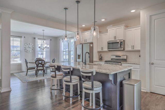 kitchen featuring stainless steel appliances, hanging light fixtures, white cabinets, a sink, and an island with sink