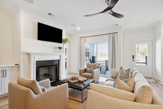 living room featuring ceiling fan, light hardwood / wood-style flooring, crown molding, and a fireplace