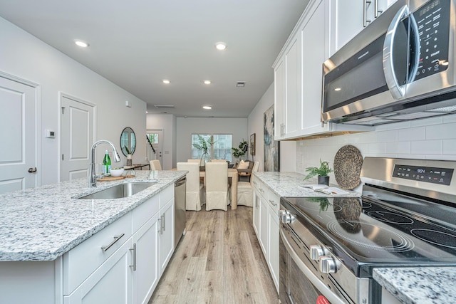 kitchen with light wood finished floors, appliances with stainless steel finishes, a sink, and white cabinetry