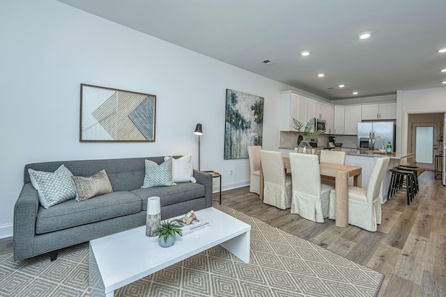 living room featuring recessed lighting, baseboards, visible vents, and light wood finished floors