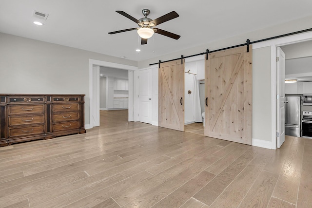 unfurnished bedroom featuring visible vents, freestanding refrigerator, light wood-style floors, baseboards, and a barn door