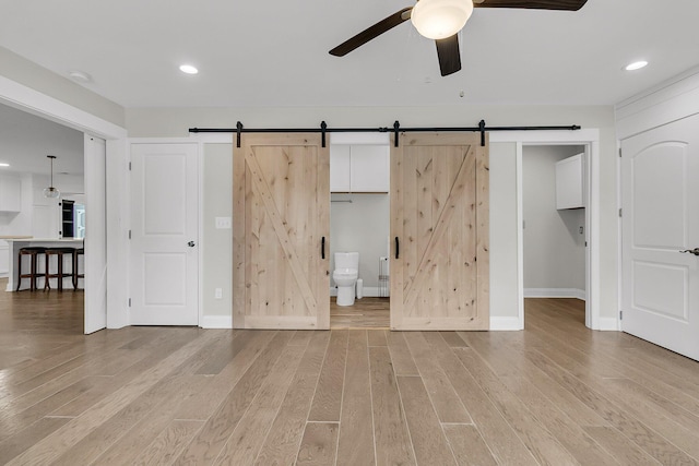unfurnished bedroom featuring a barn door, baseboards, light wood finished floors, connected bathroom, and recessed lighting