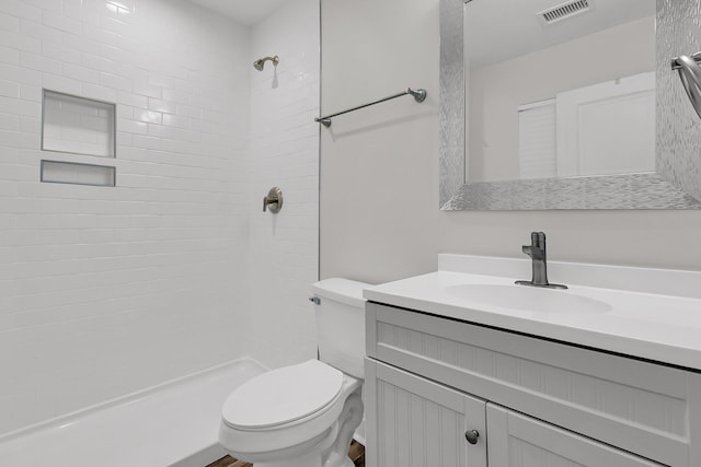 full bathroom with visible vents, tiled shower, toilet, and vanity