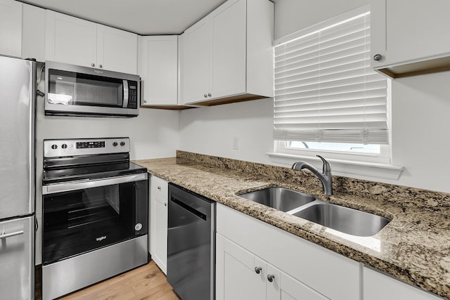 kitchen featuring light stone countertops, light wood-style floors, white cabinets, a sink, and stainless steel appliances