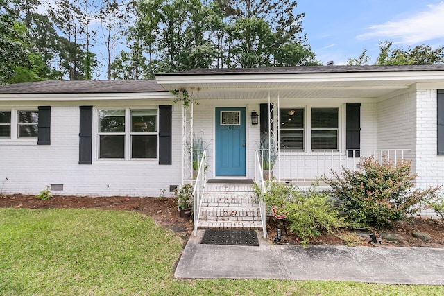 view of front of property with brick siding, a front lawn, covered porch, and crawl space