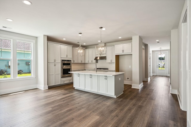 kitchen with tasteful backsplash, visible vents, double oven, light countertops, and dark wood-style flooring