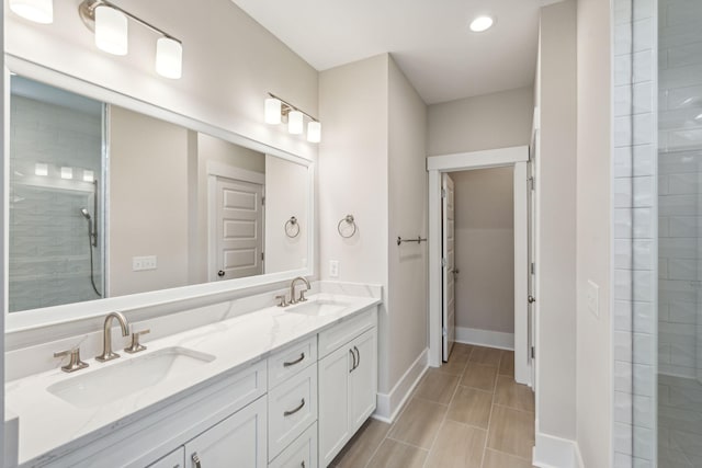 full bathroom featuring double vanity, a tile shower, baseboards, and a sink