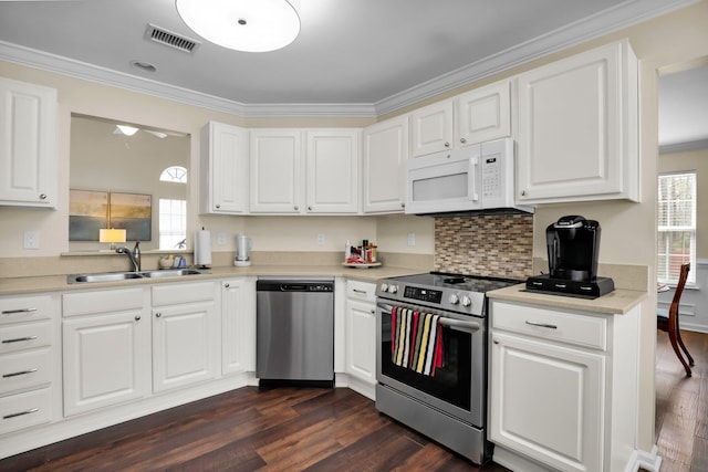 kitchen featuring visible vents, a sink, ornamental molding, stainless steel appliances, and dark wood-style flooring