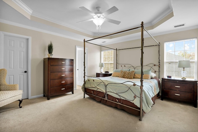 bedroom with a tray ceiling, visible vents, light colored carpet, and crown molding