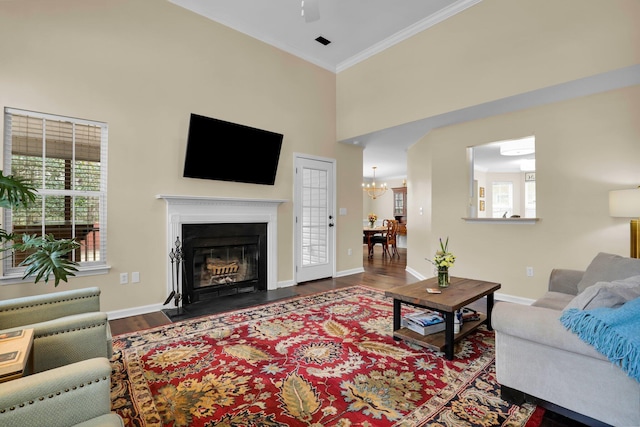 living area featuring crown molding, baseboards, a fireplace with flush hearth, a towering ceiling, and wood finished floors