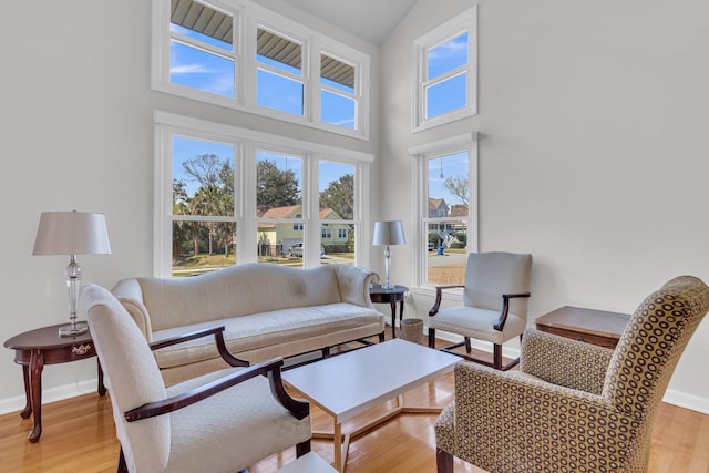 living room with light wood-type flooring, a high ceiling, and baseboards