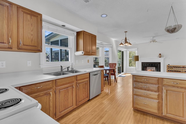 kitchen featuring light wood finished floors, light countertops, a sink, a warm lit fireplace, and dishwasher