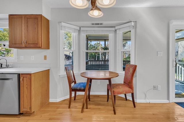 kitchen with light wood finished floors, plenty of natural light, brown cabinets, light countertops, and stainless steel dishwasher