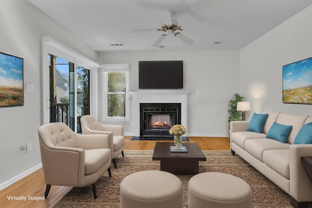 living area featuring a fireplace with flush hearth, wood finished floors, visible vents, and baseboards