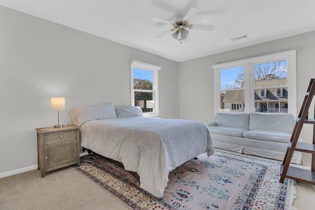 bedroom with ceiling fan, a textured ceiling, light carpet, visible vents, and baseboards