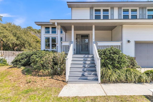 view of exterior entry with a garage, fence, and a porch