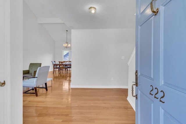 interior space featuring baseboards, lofted ceiling, a textured ceiling, light wood-type flooring, and a chandelier